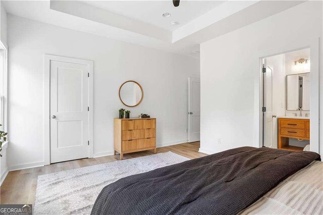 bedroom featuring a tray ceiling, ensuite bath, baseboards, and wood finished floors