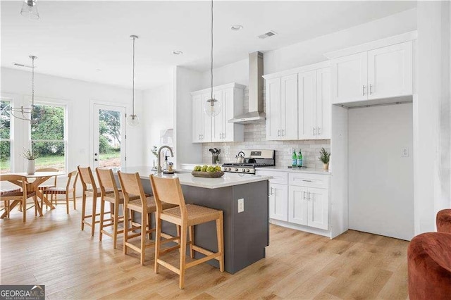 kitchen with visible vents, white cabinetry, stainless steel range oven, backsplash, and wall chimney exhaust hood