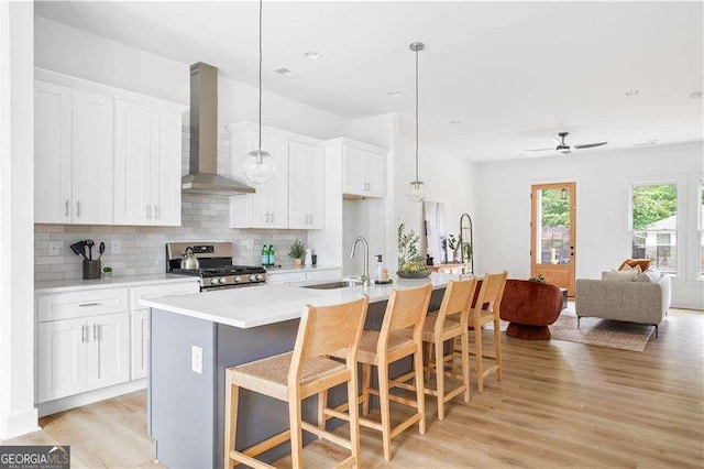 kitchen with decorative backsplash, wall chimney exhaust hood, light wood-style flooring, stainless steel gas range, and a sink