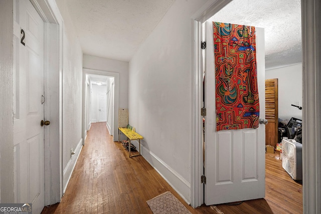 corridor with a textured ceiling, hardwood / wood-style flooring, and baseboards