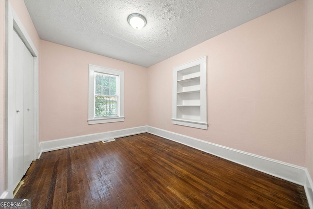 unfurnished bedroom with a textured ceiling, visible vents, baseboards, a closet, and dark wood-style floors