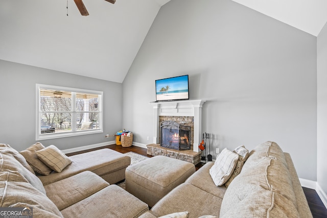 living room with baseboards, dark wood finished floors, ceiling fan, a stone fireplace, and high vaulted ceiling