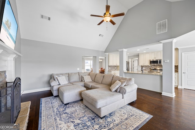 living area featuring dark wood-type flooring, visible vents, a fireplace with raised hearth, and decorative columns