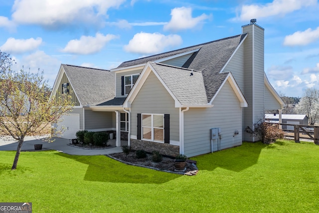 rear view of house with a shingled roof, concrete driveway, stone siding, fence, and a yard