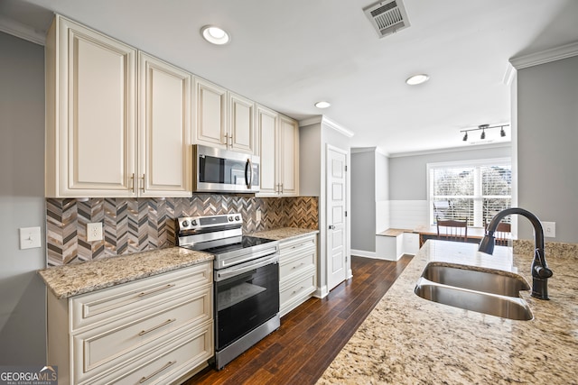 kitchen featuring visible vents, ornamental molding, stainless steel appliances, cream cabinetry, and a sink