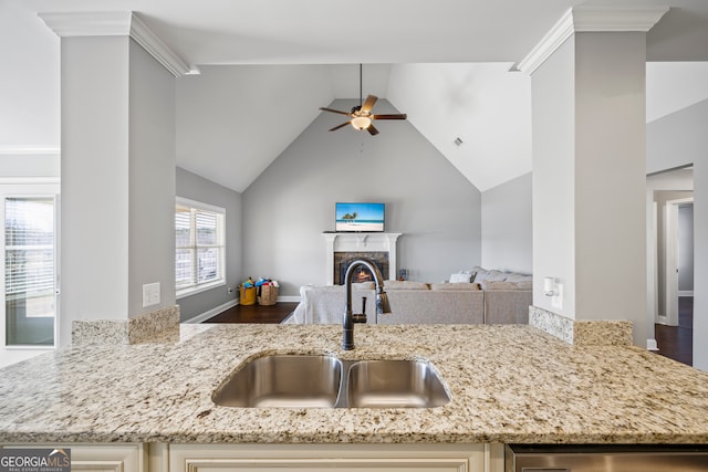 kitchen with a lit fireplace, light stone counters, open floor plan, and a sink