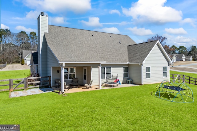 rear view of property with a shingled roof, a patio area, fence, and a lawn