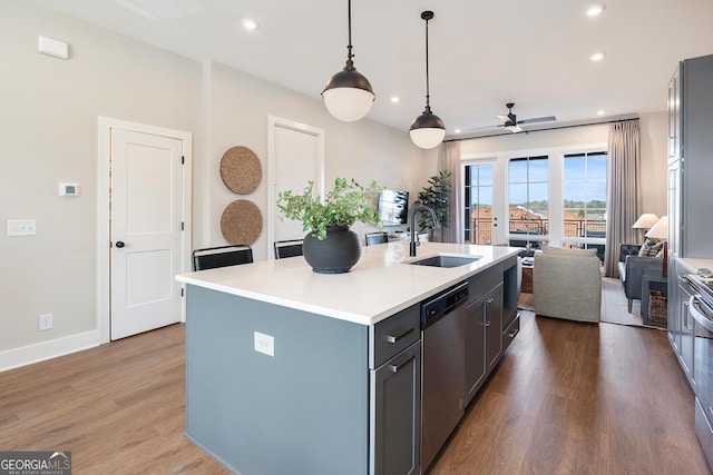 kitchen with open floor plan, wood finished floors, a sink, light countertops, and stainless steel dishwasher