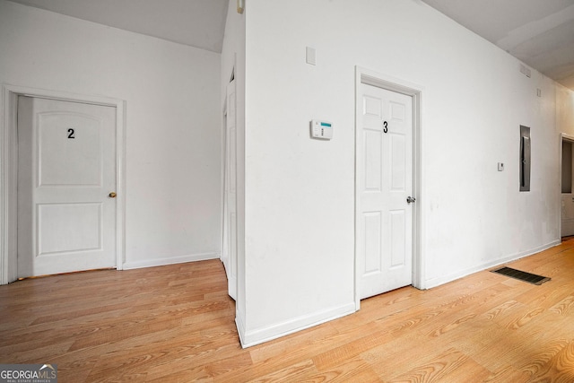 hallway with light wood-style floors, baseboards, electric panel, and visible vents