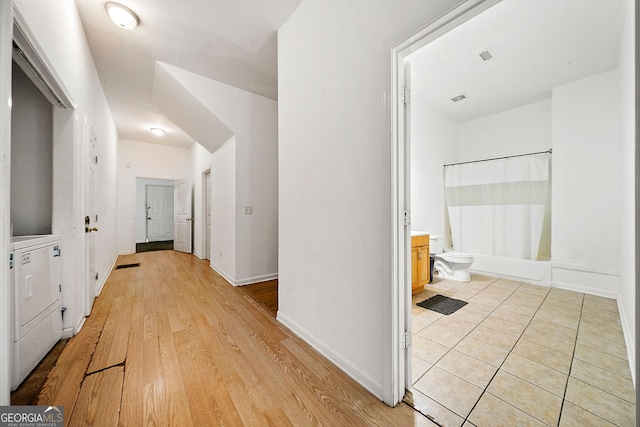 hallway with washer / clothes dryer, light wood-style flooring, visible vents, and baseboards