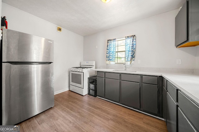 kitchen with light wood-style flooring, gray cabinetry, freestanding refrigerator, a sink, and white range with gas stovetop