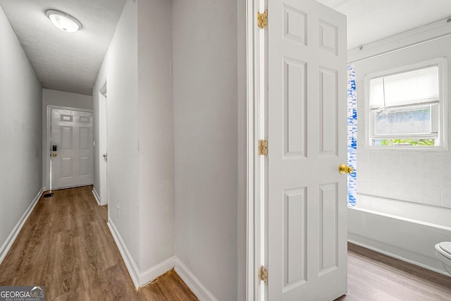 hall with a textured ceiling, wood finished floors, and baseboards