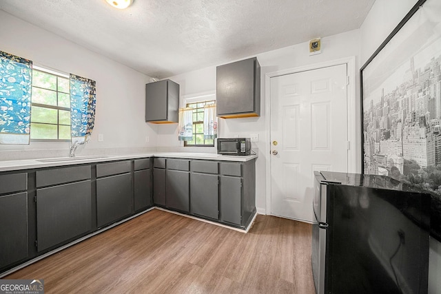 kitchen with black microwave, a textured ceiling, gray cabinetry, a sink, and light wood-style floors