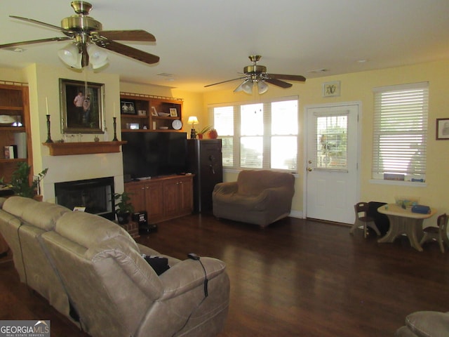 living room with a ceiling fan, a glass covered fireplace, and dark wood finished floors