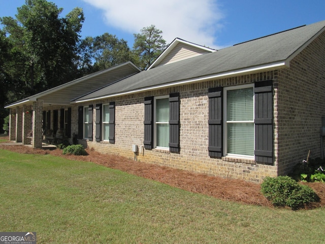 exterior space featuring a shingled roof, a lawn, and brick siding