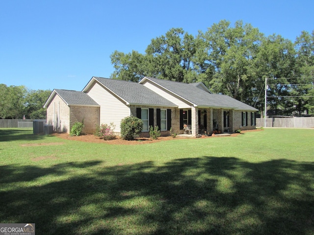 view of front of property with central AC, brick siding, fence, roof with shingles, and a front lawn