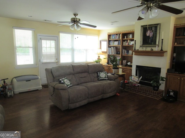 living area with a brick fireplace, ceiling fan, visible vents, and dark wood-style flooring