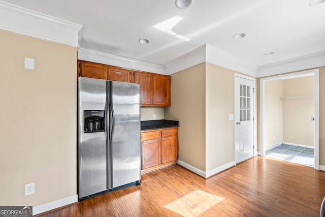 kitchen with brown cabinets, dark countertops, ornamental molding, light wood-type flooring, and stainless steel fridge with ice dispenser