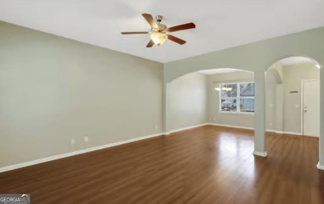 unfurnished living room with a ceiling fan, arched walkways, baseboards, and wood finished floors