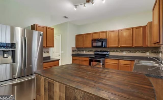 kitchen with tasteful backsplash, brown cabinetry, butcher block counters, appliances with stainless steel finishes, and a sink