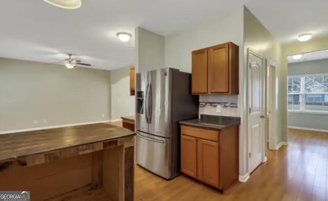 kitchen with a ceiling fan, dark countertops, light wood-style flooring, brown cabinets, and stainless steel refrigerator with ice dispenser