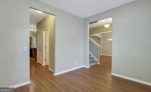 empty room with arched walkways, stairway, wood finished floors, and baseboards