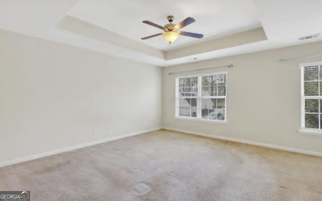 spare room with a ceiling fan, carpet, a raised ceiling, and baseboards