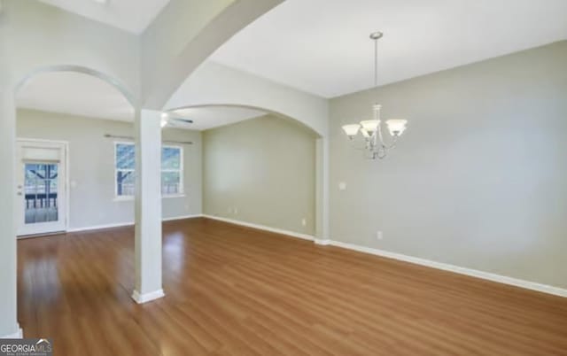 interior space featuring arched walkways, a notable chandelier, baseboards, and wood finished floors