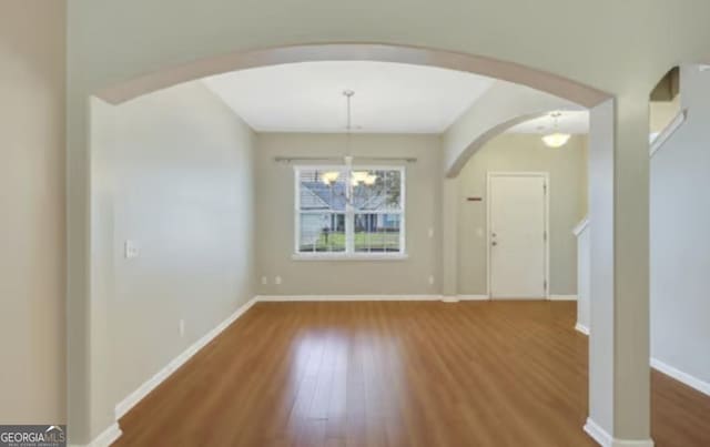 unfurnished dining area featuring baseboards, arched walkways, a chandelier, and wood finished floors