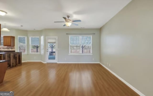 unfurnished living room with ceiling fan, baseboards, and wood finished floors