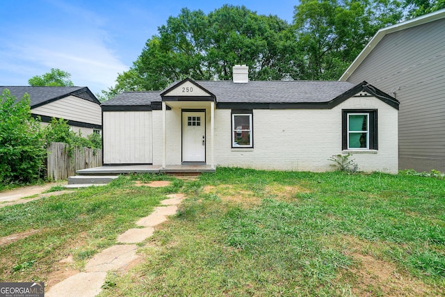 view of front of house with a chimney, roof with shingles, fence, a front lawn, and brick siding