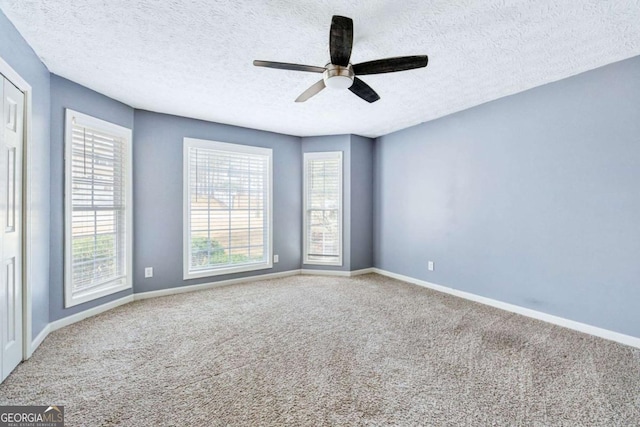 carpeted spare room featuring a textured ceiling, a ceiling fan, and baseboards