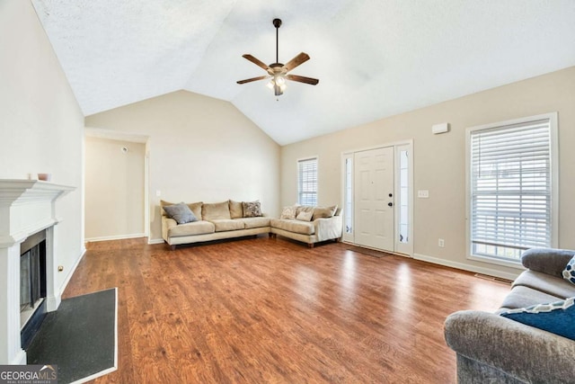 living area featuring lofted ceiling, wood finished floors, a glass covered fireplace, and a ceiling fan