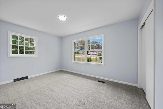 unfurnished bedroom featuring multiple windows, carpet flooring, visible vents, and baseboards