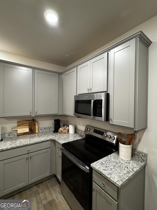 kitchen featuring light stone countertops, gray cabinets, stainless steel appliances, and dark wood-style flooring