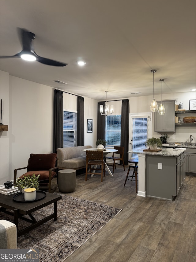 living area featuring visible vents, dark wood finished floors, and ceiling fan with notable chandelier