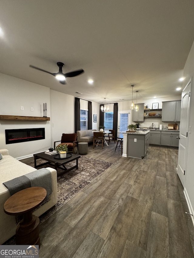 living area with dark wood-style floors, ceiling fan with notable chandelier, and a glass covered fireplace