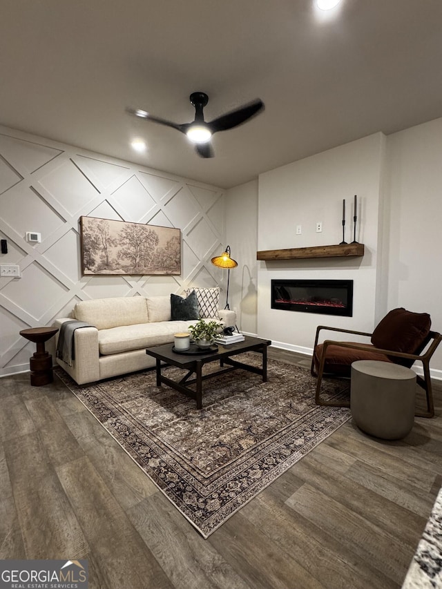 living room featuring ceiling fan, baseboards, wood finished floors, and a glass covered fireplace