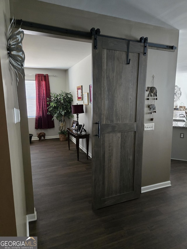 hall featuring dark wood-style floors, baseboards, and a barn door