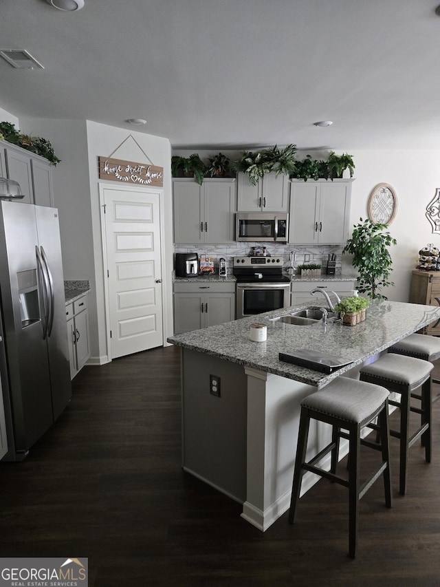 kitchen featuring a breakfast bar area, light stone counters, a sink, decorative backsplash, and appliances with stainless steel finishes