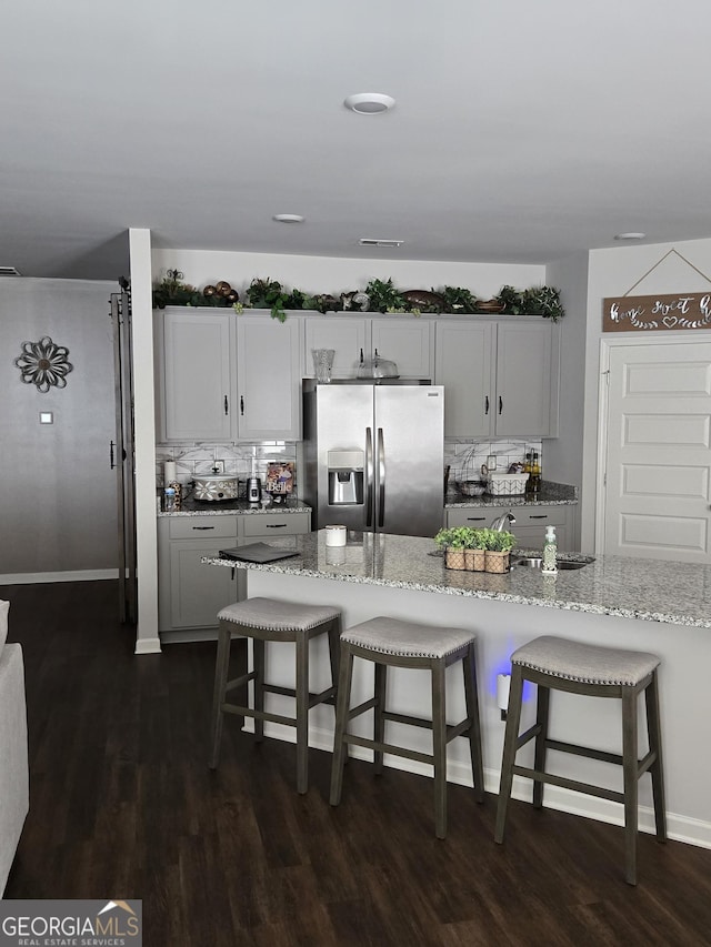 kitchen featuring dark wood finished floors, light stone counters, a breakfast bar area, and stainless steel refrigerator with ice dispenser