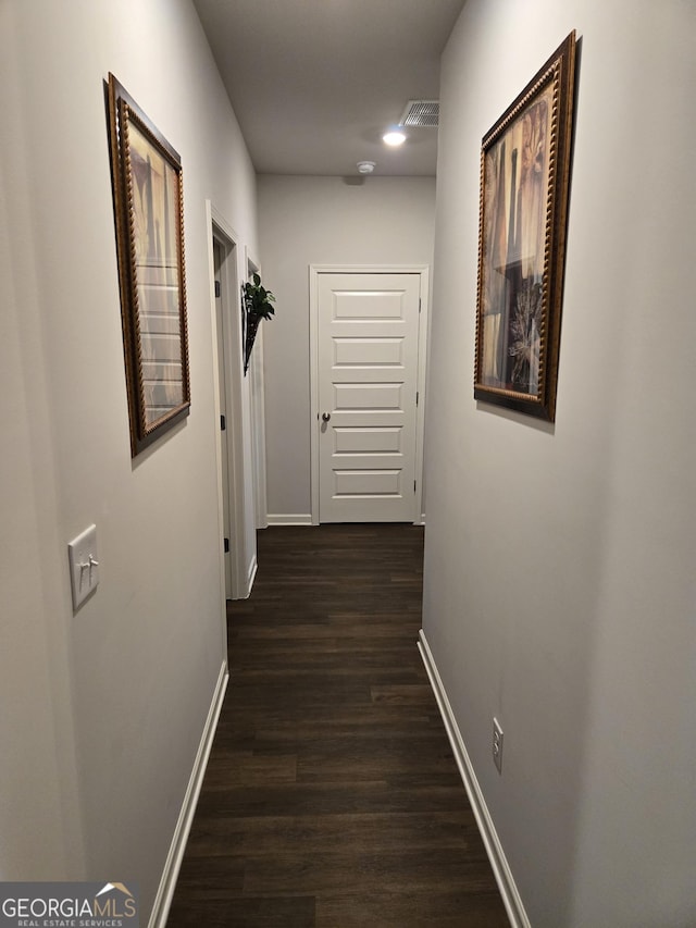 hall with visible vents, baseboards, and dark wood-type flooring