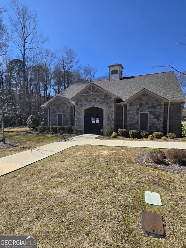 view of front of property with a front lawn, stone siding, driveway, and roof with shingles