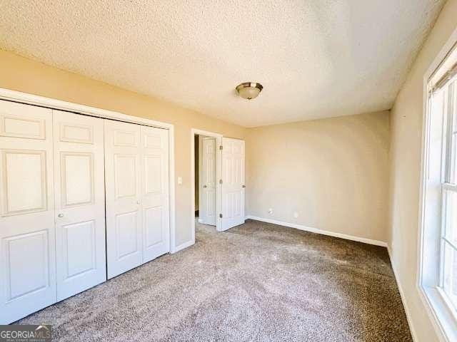 unfurnished bedroom featuring a textured ceiling, a closet, carpet flooring, and baseboards