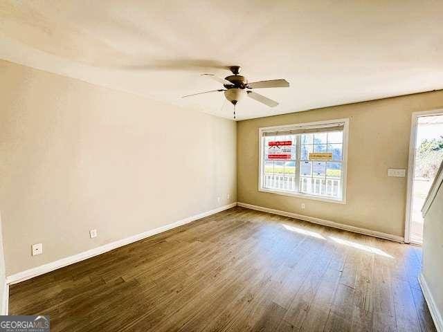 empty room featuring a healthy amount of sunlight, ceiling fan, baseboards, and wood finished floors