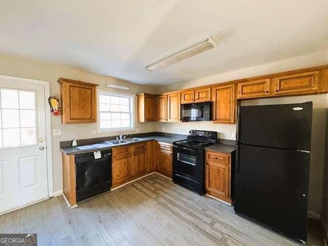 kitchen featuring dark countertops, black appliances, brown cabinetry, and a sink