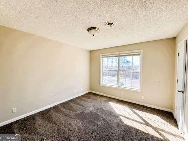 empty room featuring dark colored carpet, visible vents, a textured ceiling, and baseboards