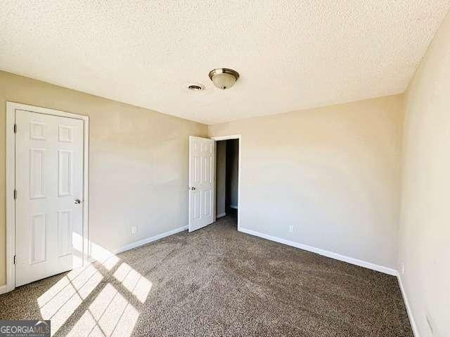 unfurnished bedroom with visible vents, a textured ceiling, baseboards, and carpet flooring