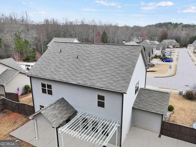 rear view of property with roof with shingles, fence, and a view of trees