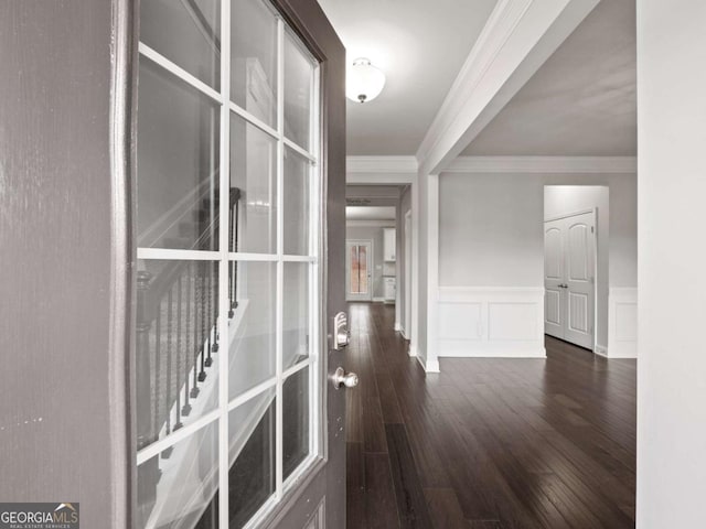 hall featuring a decorative wall, wainscoting, dark wood finished floors, and crown molding